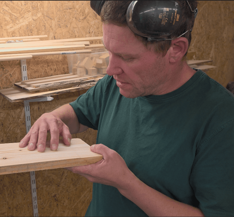 Hände bearbeiten ein Stück Holz mit einem Handhobel, feine Späne fallen herab