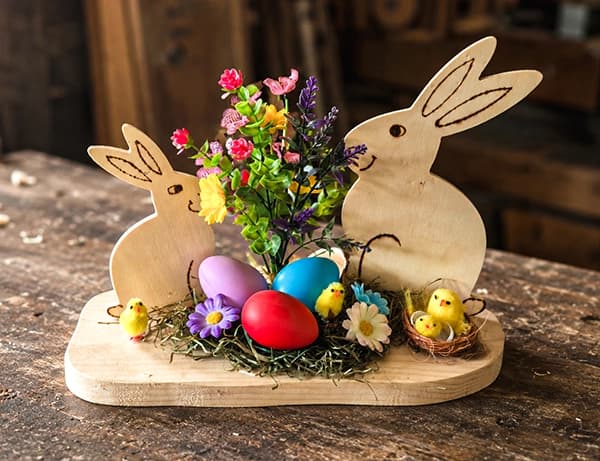 Osterdekoration aus Holz mit zwei Hasen, bunten Eiern, Blumen und kleinen Küken