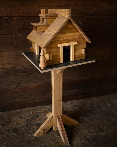 Aufwendig gebautes Vogelhaus als kleine Holzvilla auf einem Standfuß